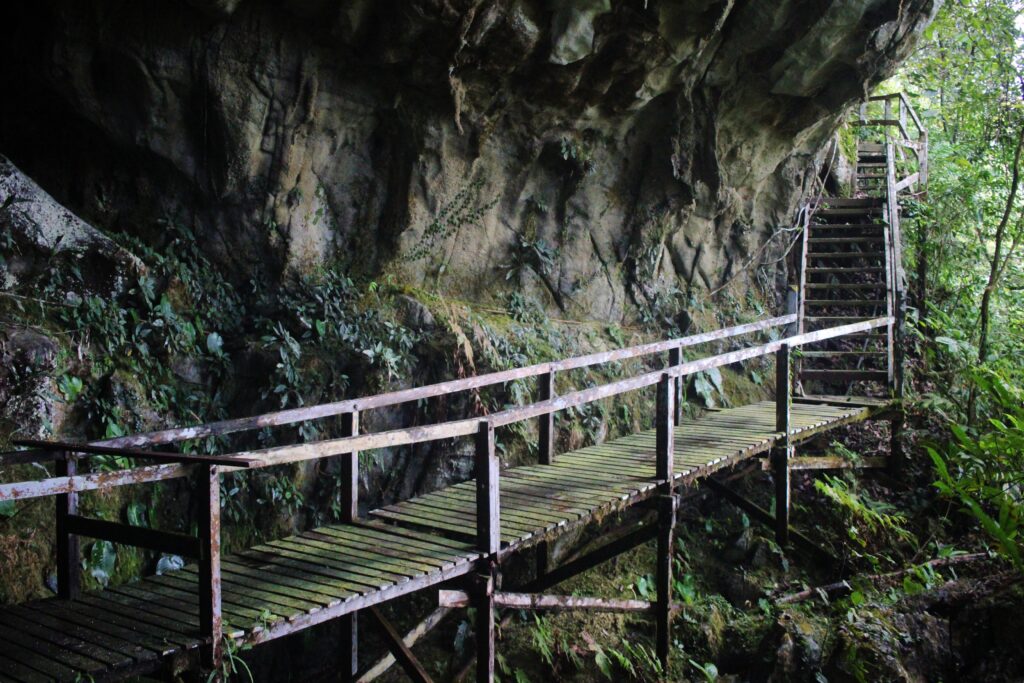 A wooden boardwalk along the side of a cave going to the outside