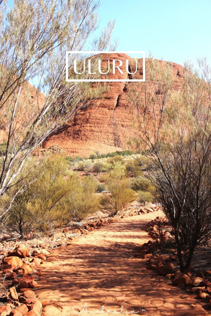 A dusty path winds around the base of Uluru