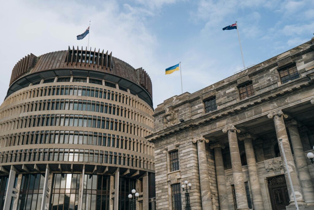 A stone building with columns in front of the circular architecture of the Beehive, Wellington's parliament