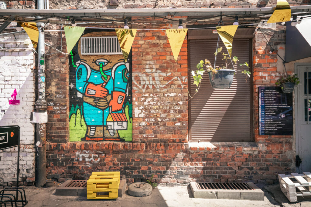 An orange brick wall with some colourful art in windows and yellow bunting