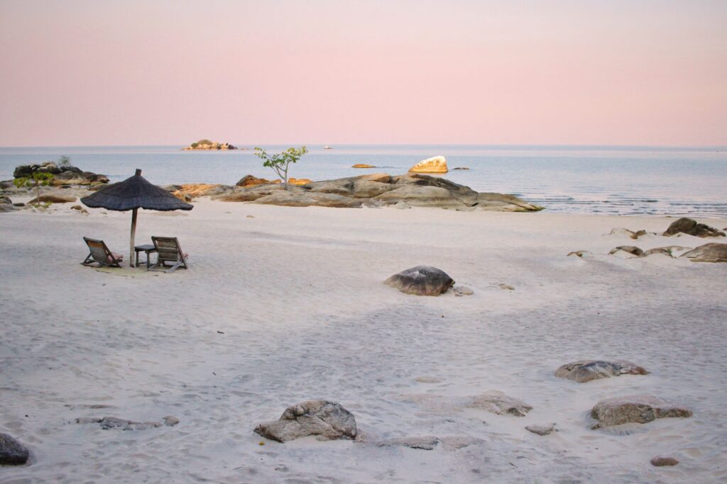 A pink pastel sunset over a white sand beach with a woven umbrella