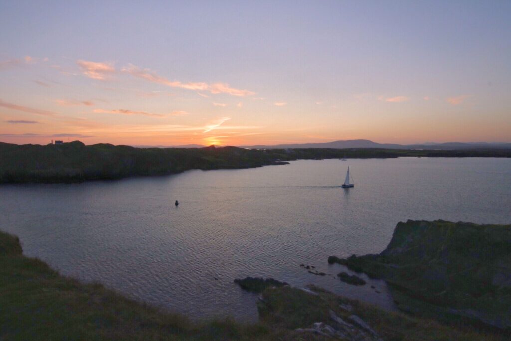 Sunset over a sea inlet, with a small yacht on the water