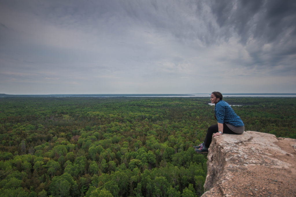 Sitting on the edge of the cliff at Manitoulin Island, one of the best places for Ontario day hikes
