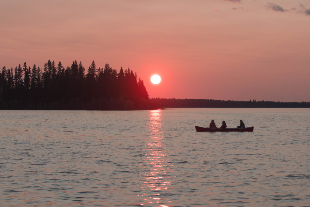 Three people sit in a canoe under a pink sunset at Elk Island National Park, Canada