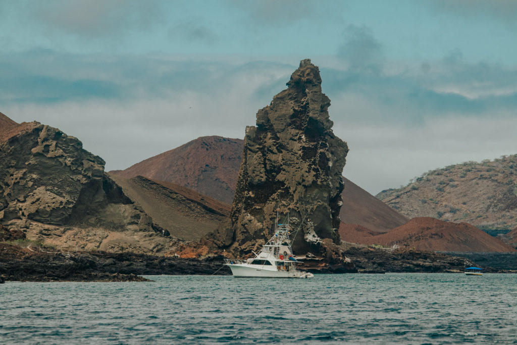 A boat floats on the water in front of Pinnacle Rock in the Galapagos