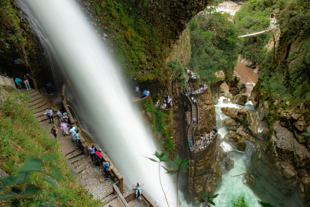 A powerful waterfall falls into a narrow canyon, past carved steps with people below