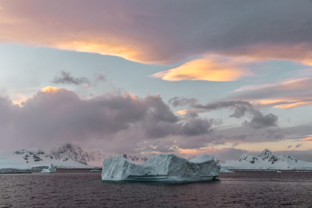 A pink sunset over a huge iceberg with mountains in the background - a novel sight to a backpacker in Antarctica
