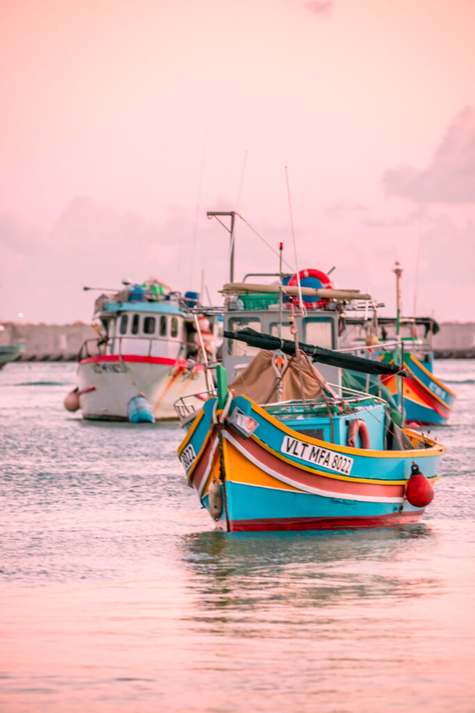 Pink skies over a traditional colourful Maltese fishing boat at anchor, Malta