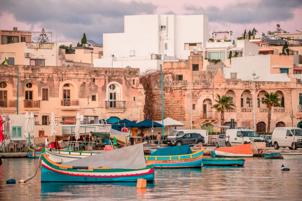 Colourful fishing boats in front of the seafront of Marsaxlokk, a small town in Malta