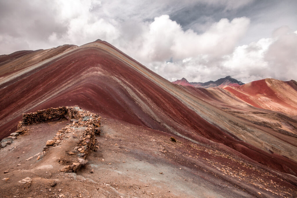 The contrasting red, yellow and brown stipes of Rainbow Mountain under a cloudy sky