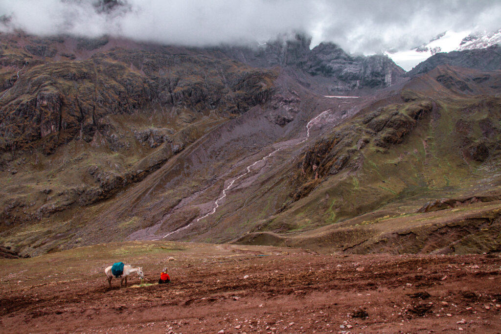A horse and Peruvian in front of a steep mountain valley bisected by a thin river in Peru