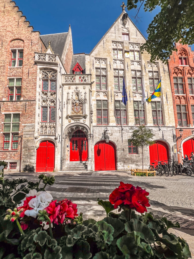 Red flowers matching the painted doors of beautiful buildings in Bruges