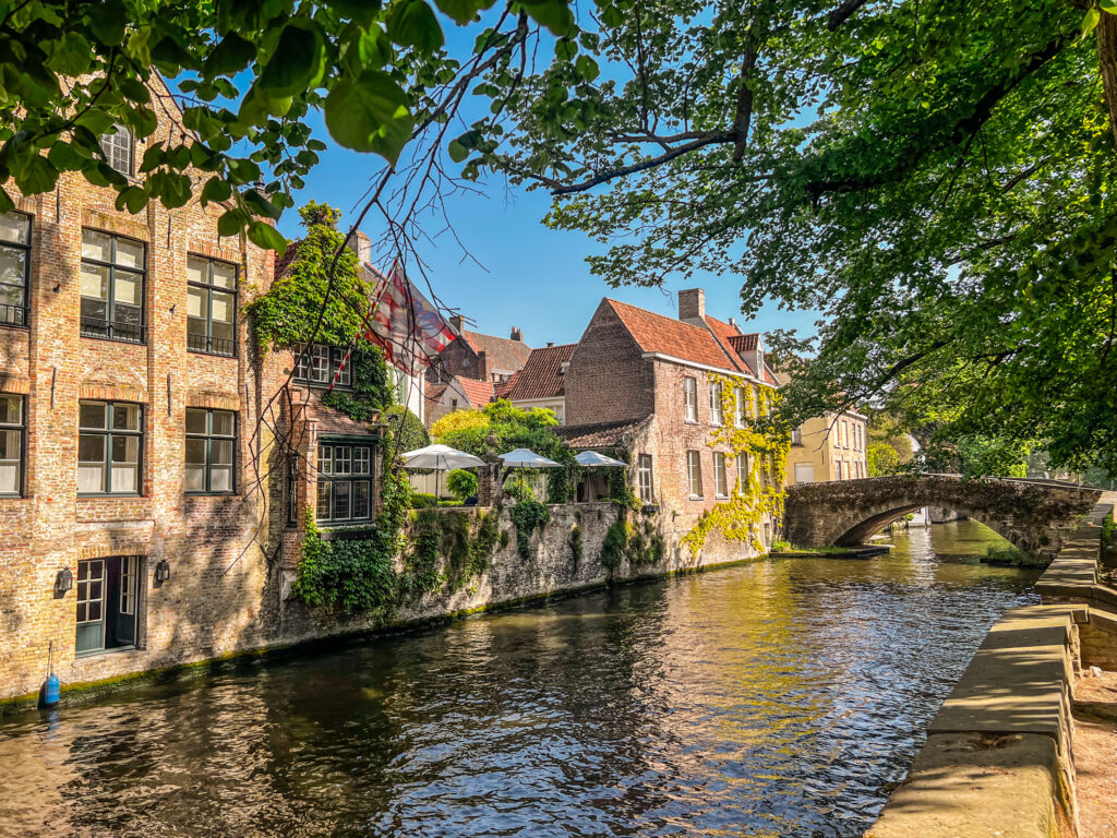 The canals of Bruges traverse the city, with beautiful architecture and leafy trees.