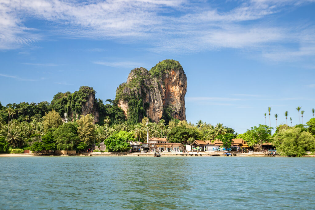 A small town by the coast with thick greenery and tall, uniquely shaped cliffs rising above 