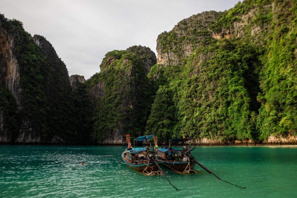A boat anchored in Pileh Lagoon, with tall, green cliffs rising all around