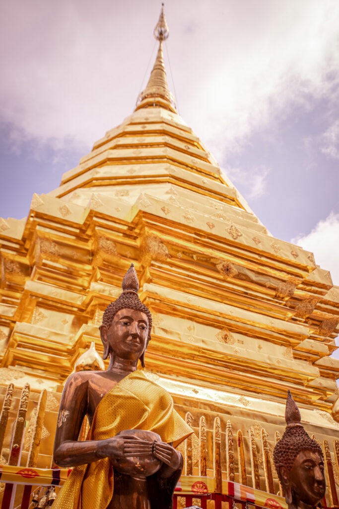 A golden temple and statue against a blue, cloudy sky