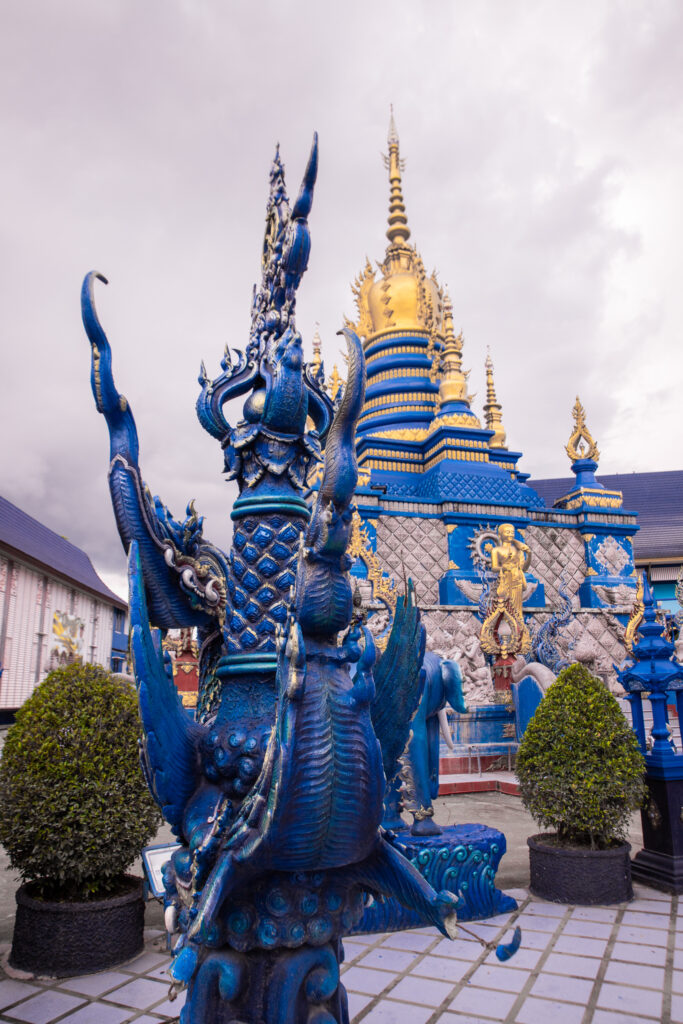 Ornate blue statue in front of a blue and gold temple in Chiang Rai