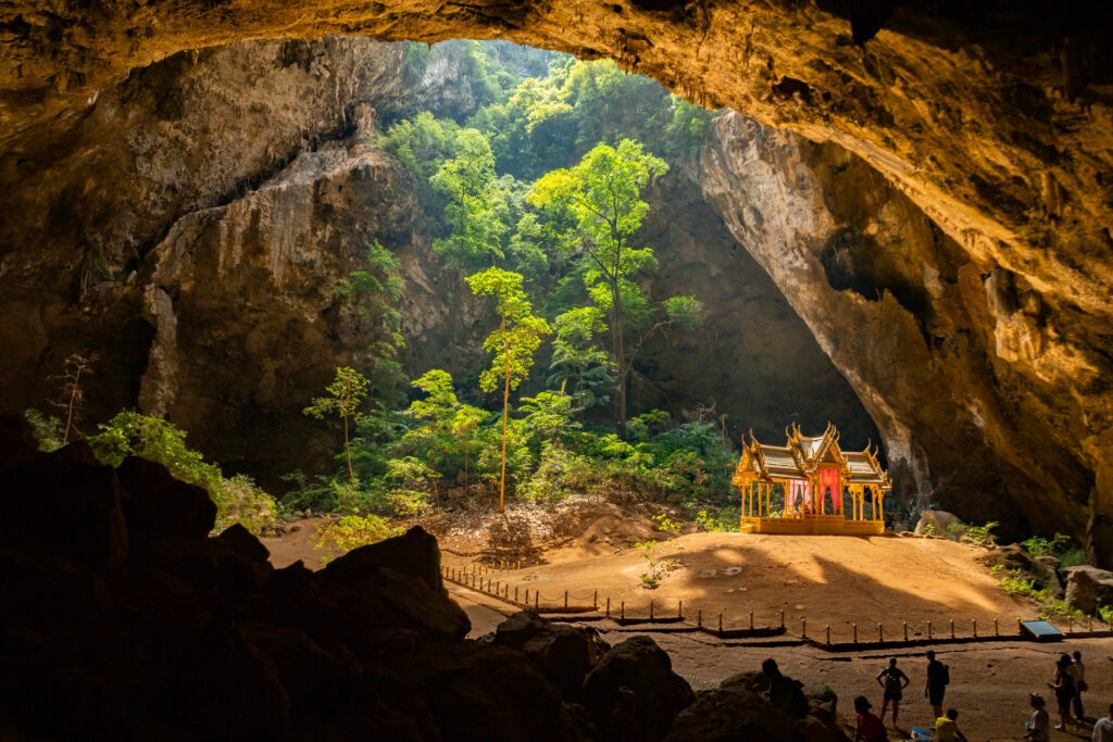 A pagoda inside a large cave with trees is illuminated by a beam of sunlight