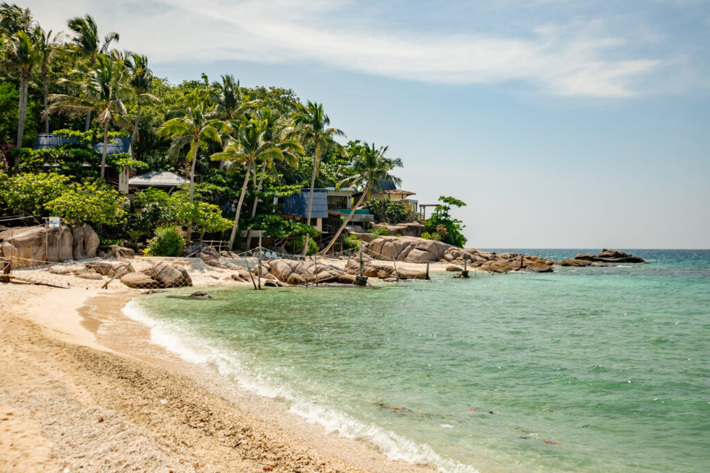 A stunning beach on a sunny day with hilly greenery rolling down to the water