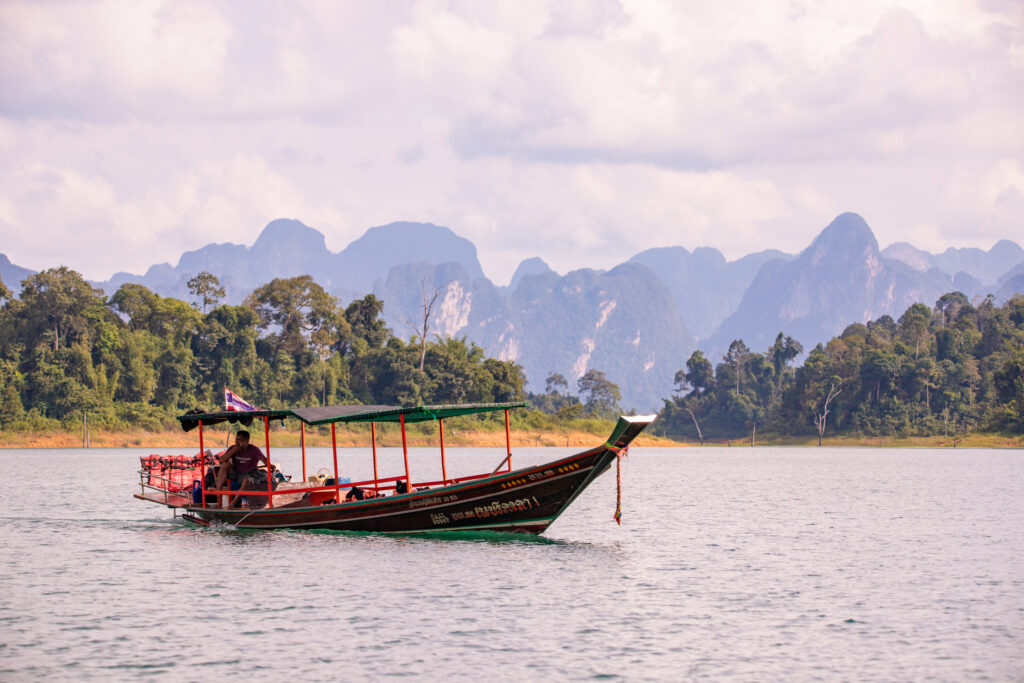 Tall mountains in the background behind islands and a boat crossing the lake in Khao Sok National Park, Thailand