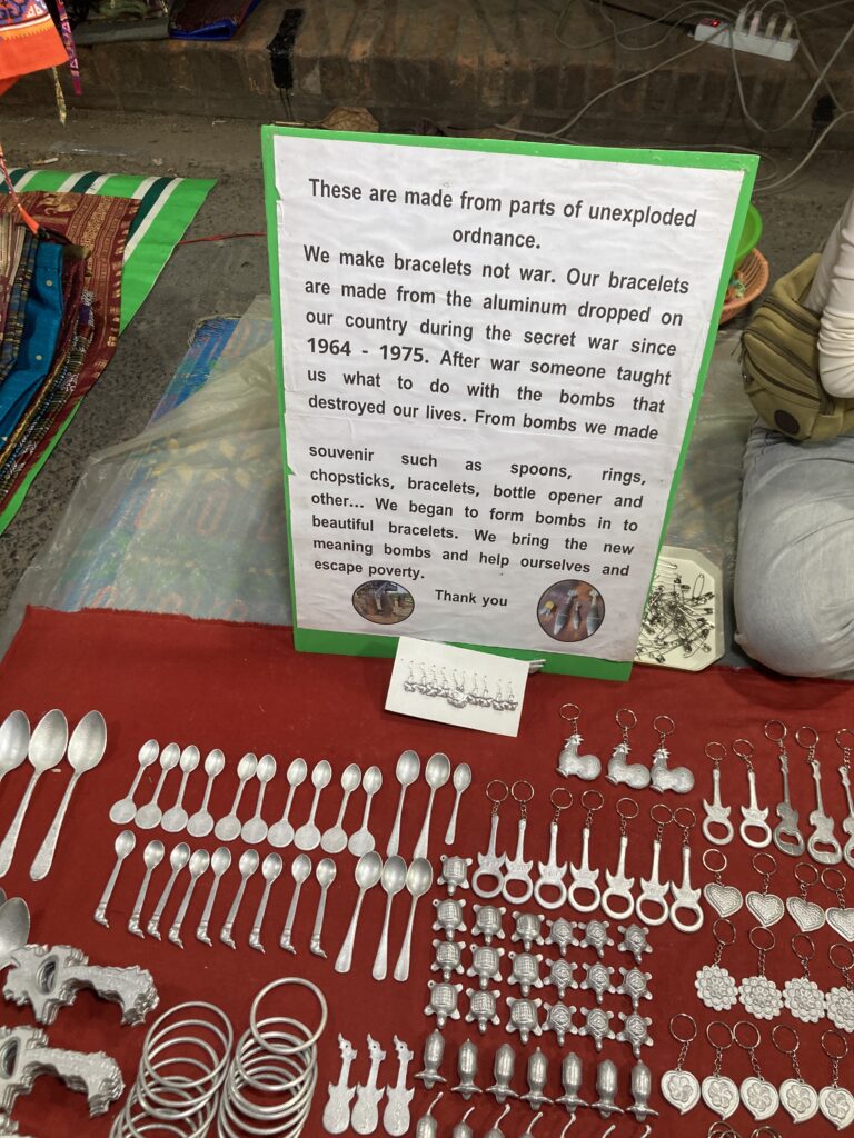 Key rings made from bomb fragments laid out on red fabric, with an explanatory sign