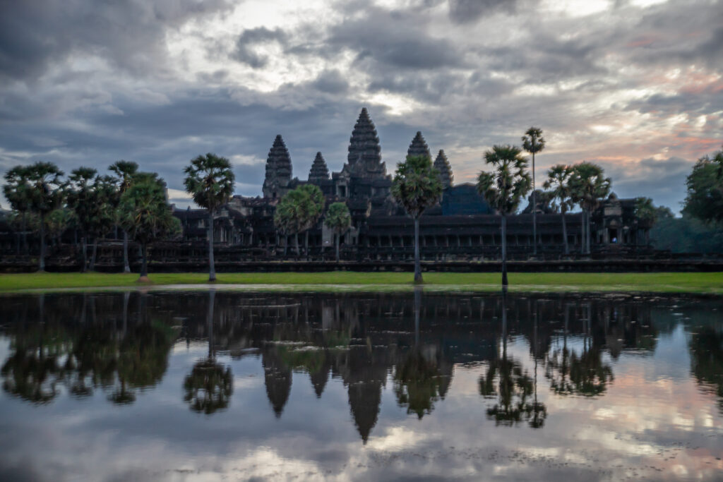 The iconic skyline of Angkor Wat silhouetted on a cloudy morning, reflected in water
