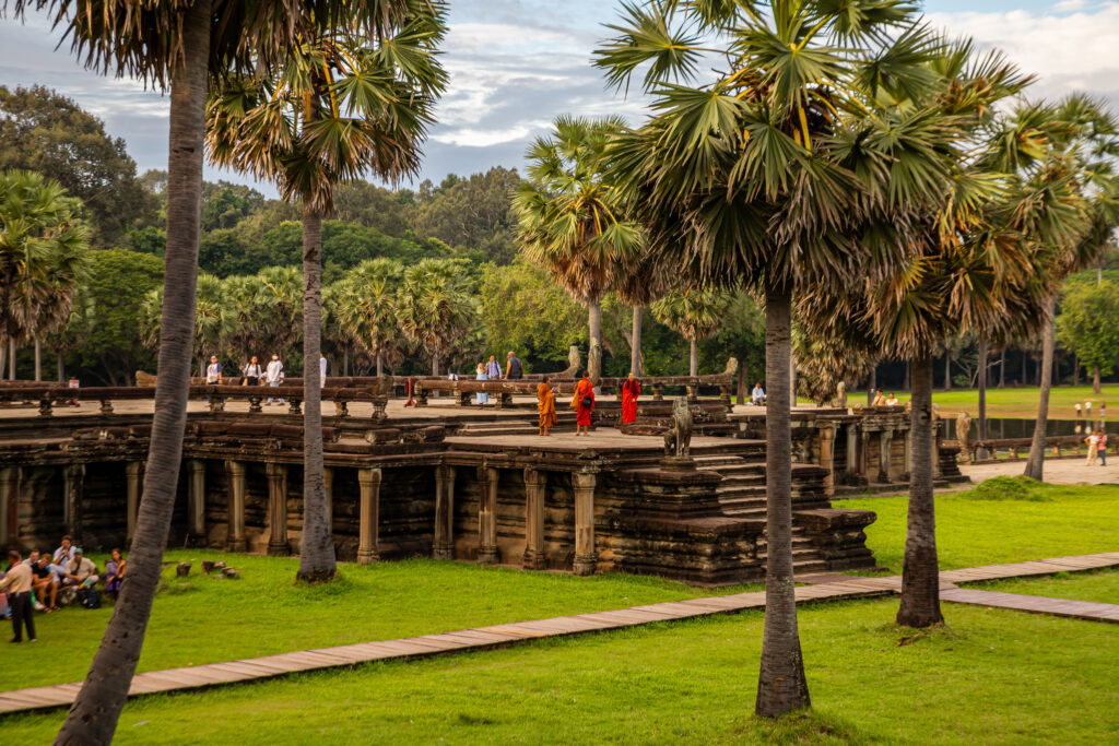 Three Buddhist monks in orange robes walk in the ruins of Angkor Wat