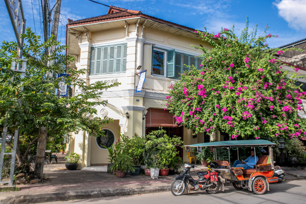 A tuk-tuk waits outside a colonial-style building with colourful flowers in Cambodia