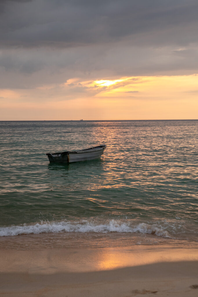 A small rowing boat floats offshore at sunset
