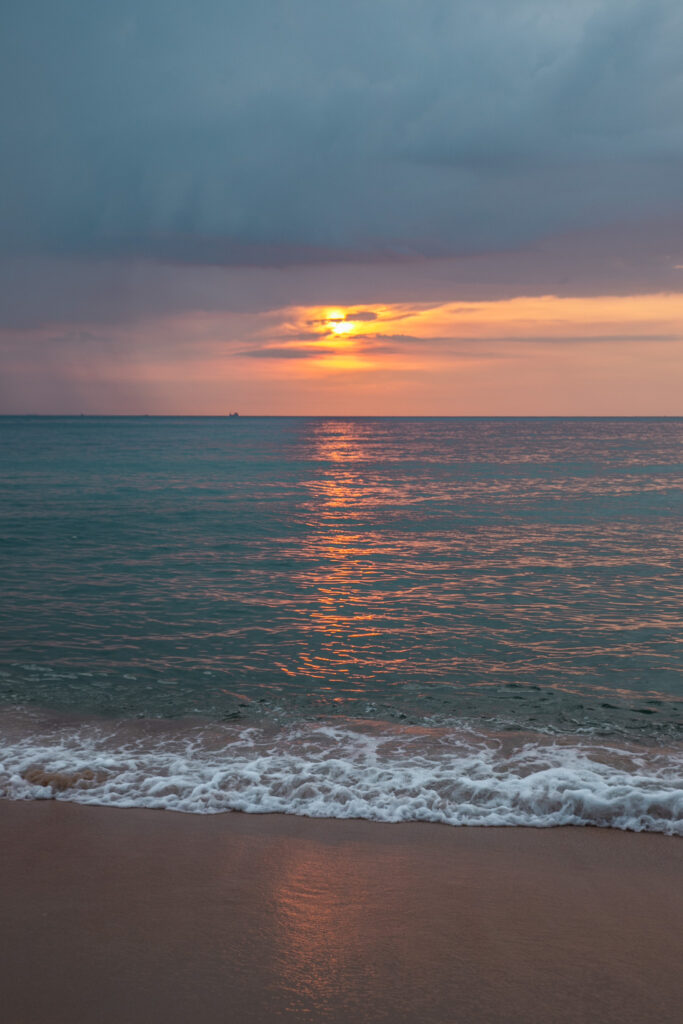 The sun sets over the water from a beach