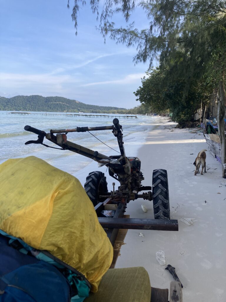 A tractor with luggage driving along a beach, half in the water