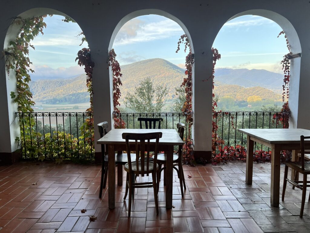 Tables sit on a veranda with stone arches overlooking rolling hills