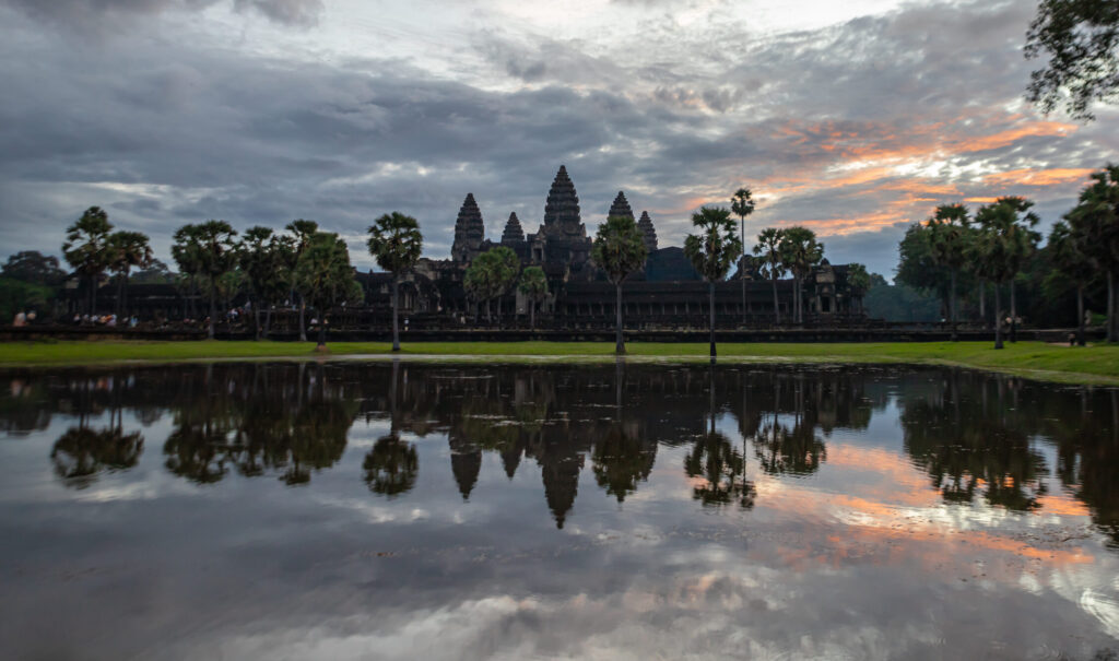 The iconic skyline of Angkor Wat silhouetted on a cloudy morning, reflected in water