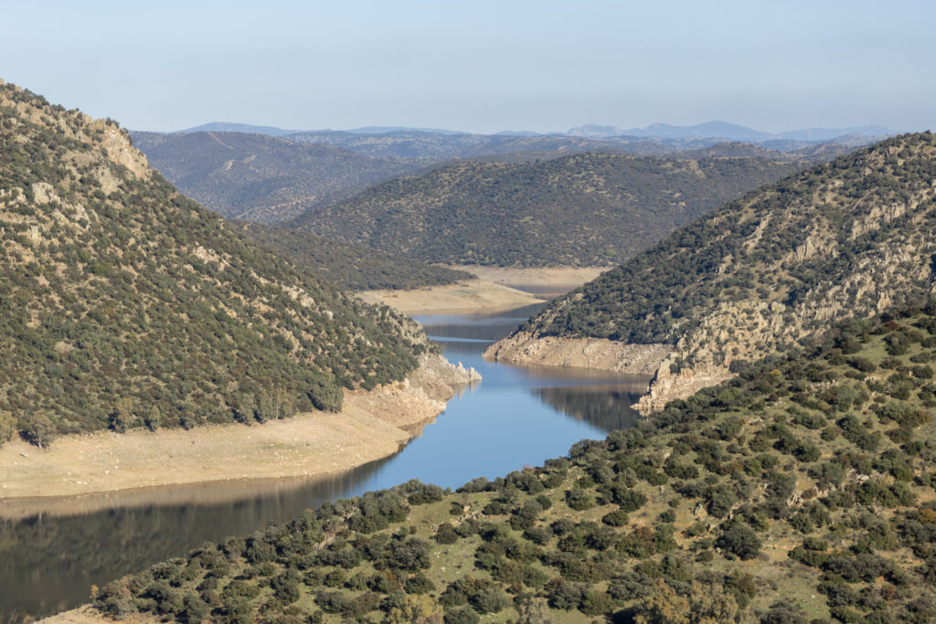 The flooded area of the river above the La Lancha dam, with green hills covered in small trees.