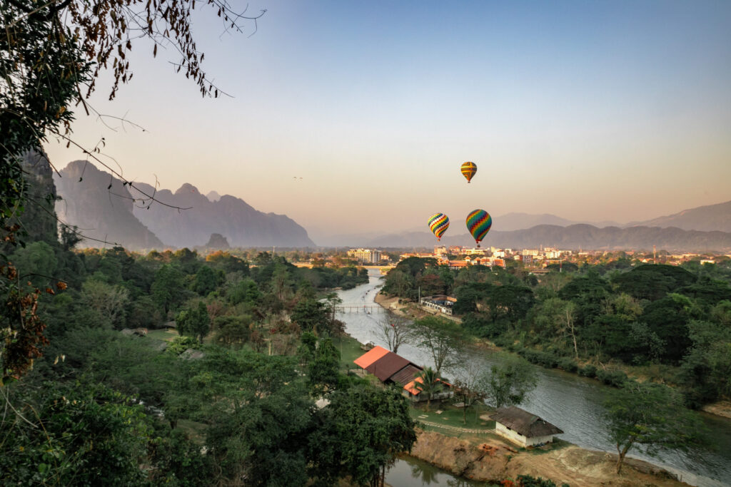 Hot air balloons in the sky at sunset over a town by a river in Laos