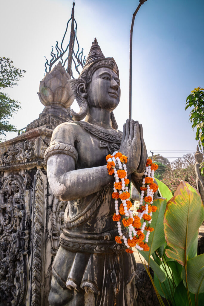 A Buddha statue with strings of orange flowers around its hands