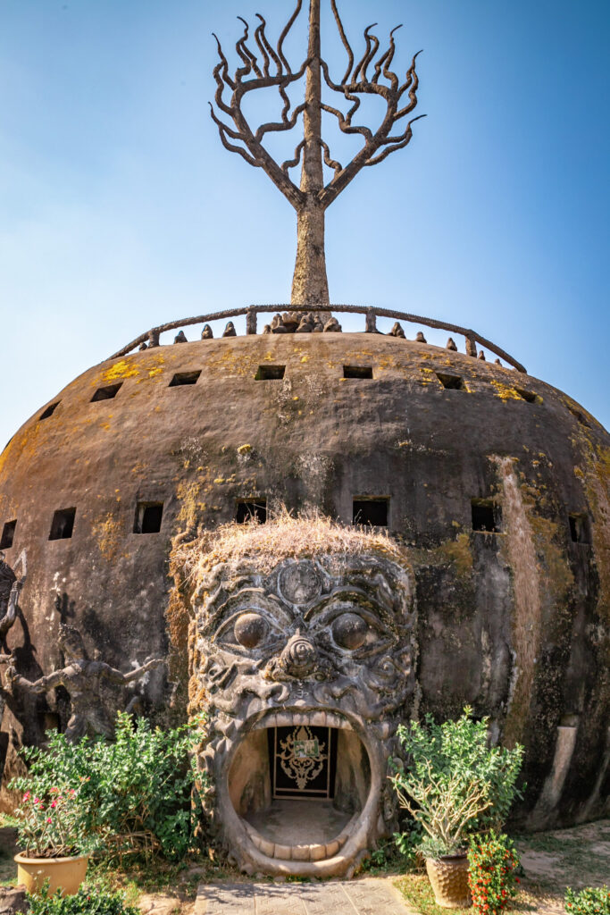 A large artificial structure with a stone tree on top and a gaping demon face as an entrance